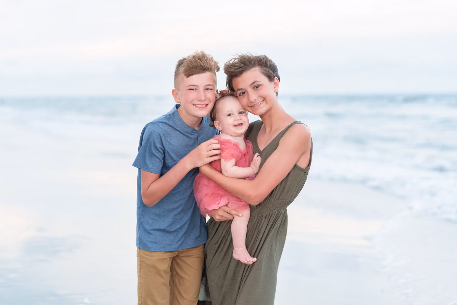 Big brother and sister holding their baby sister between them by the ocean at Huntington Beach State Park