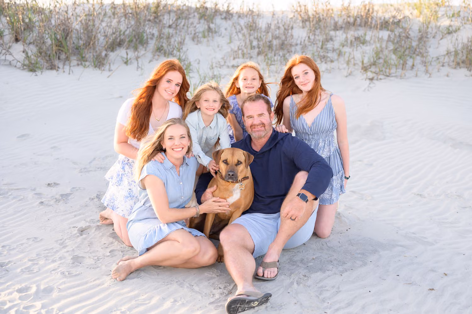 Family of six sitting together in the sand with their dog in front of the dunes in Sunset Beach
