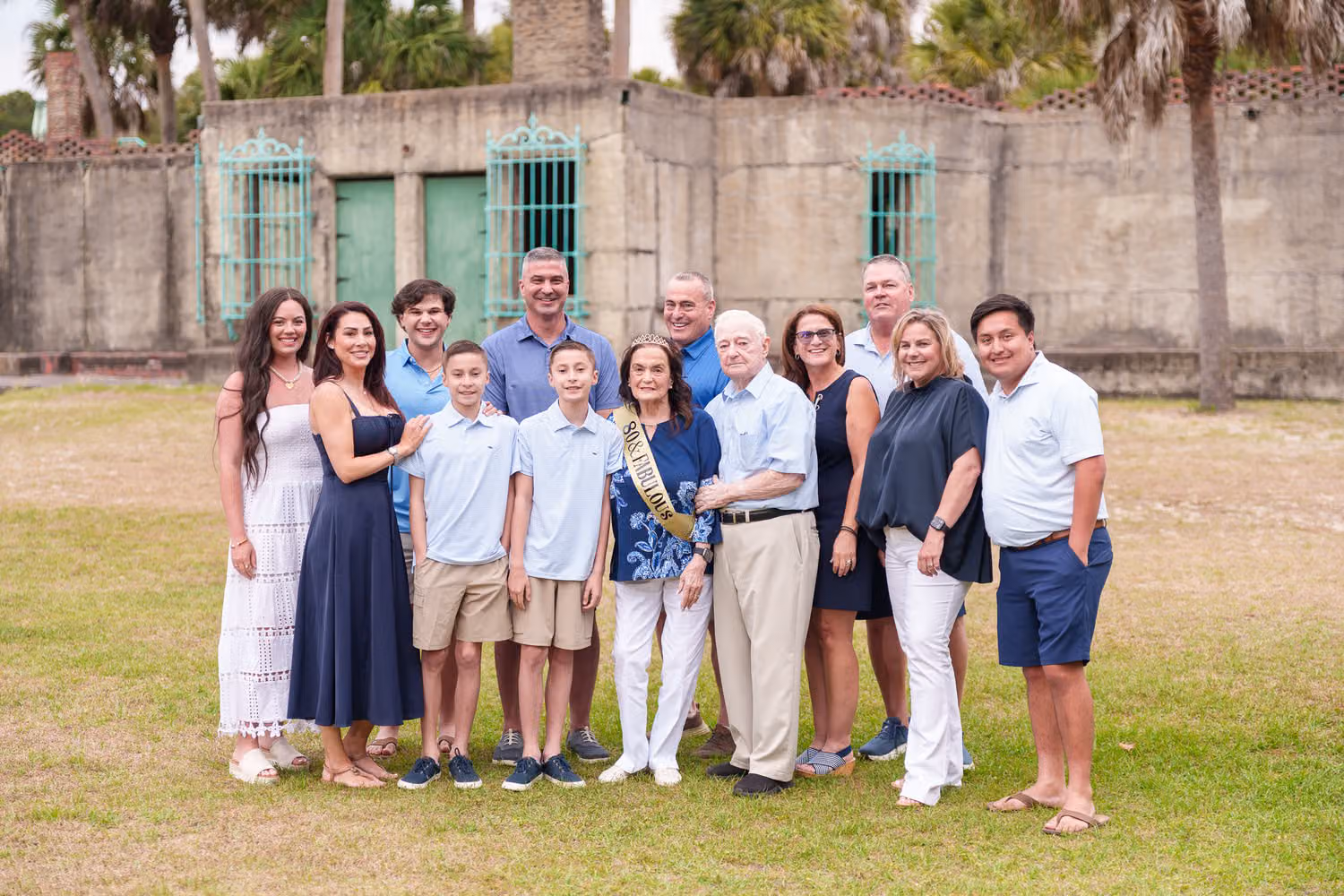 Extended family around a woman in a birthday sash in front of the Atalaya Castle walls at Huntington Beach State Park