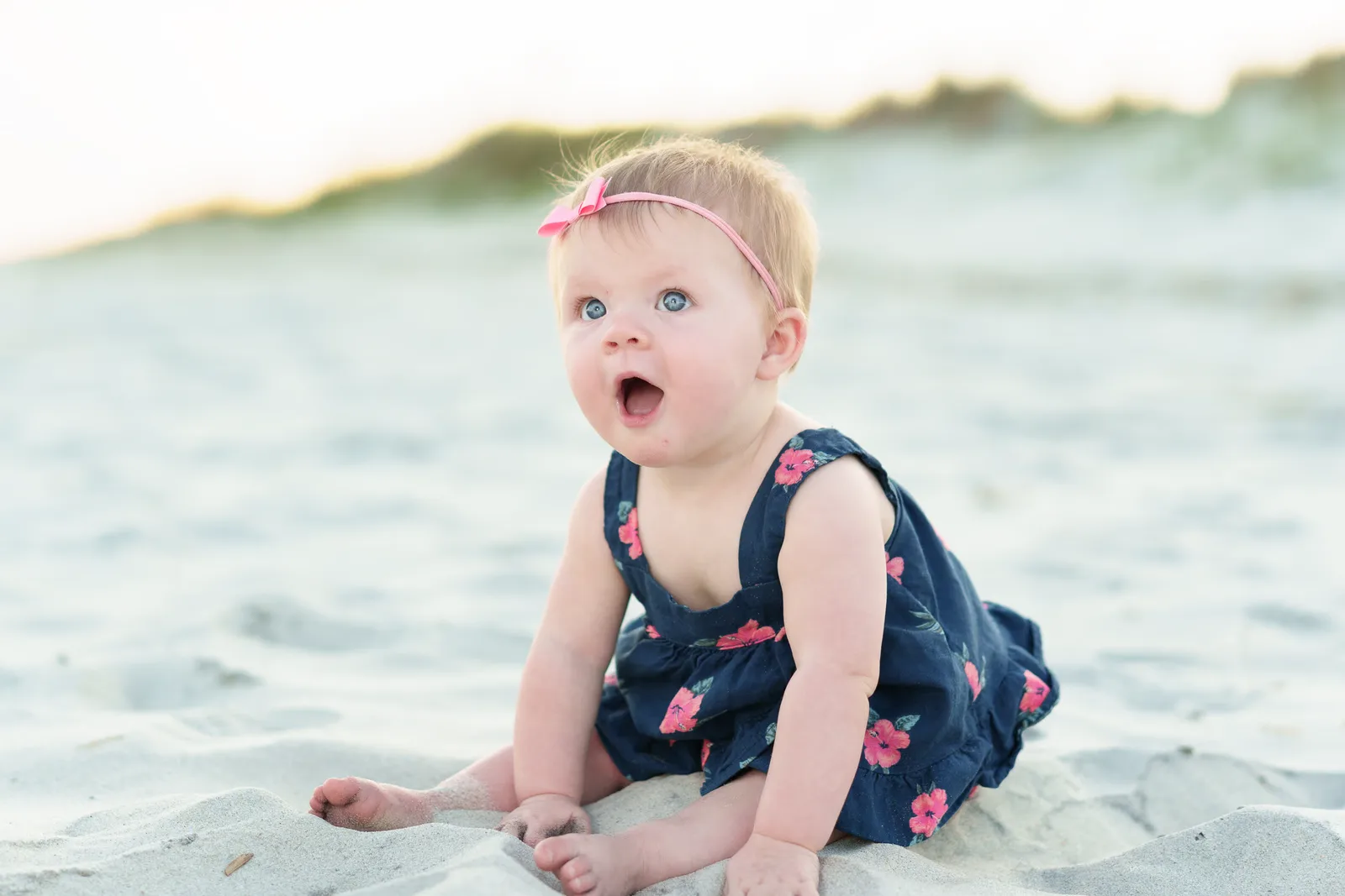 Baby girl with big blue eyes sitting by the ocean -