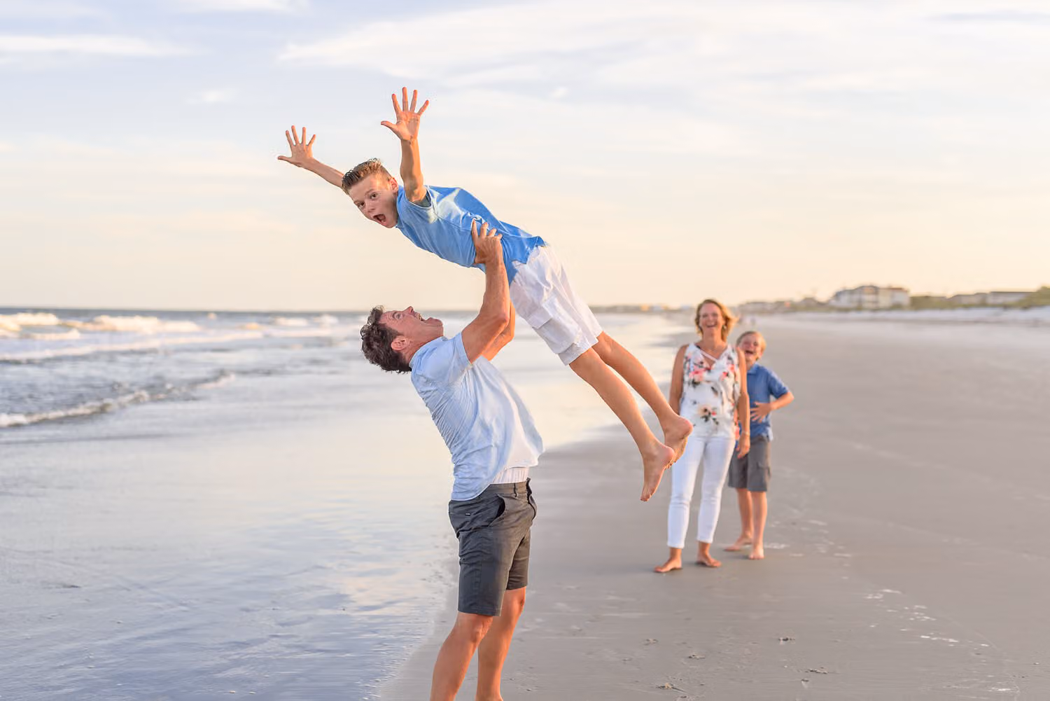 Dad tossing his son high into the air on the beach while mom and a younger child watch at Myrtle Beach State Park