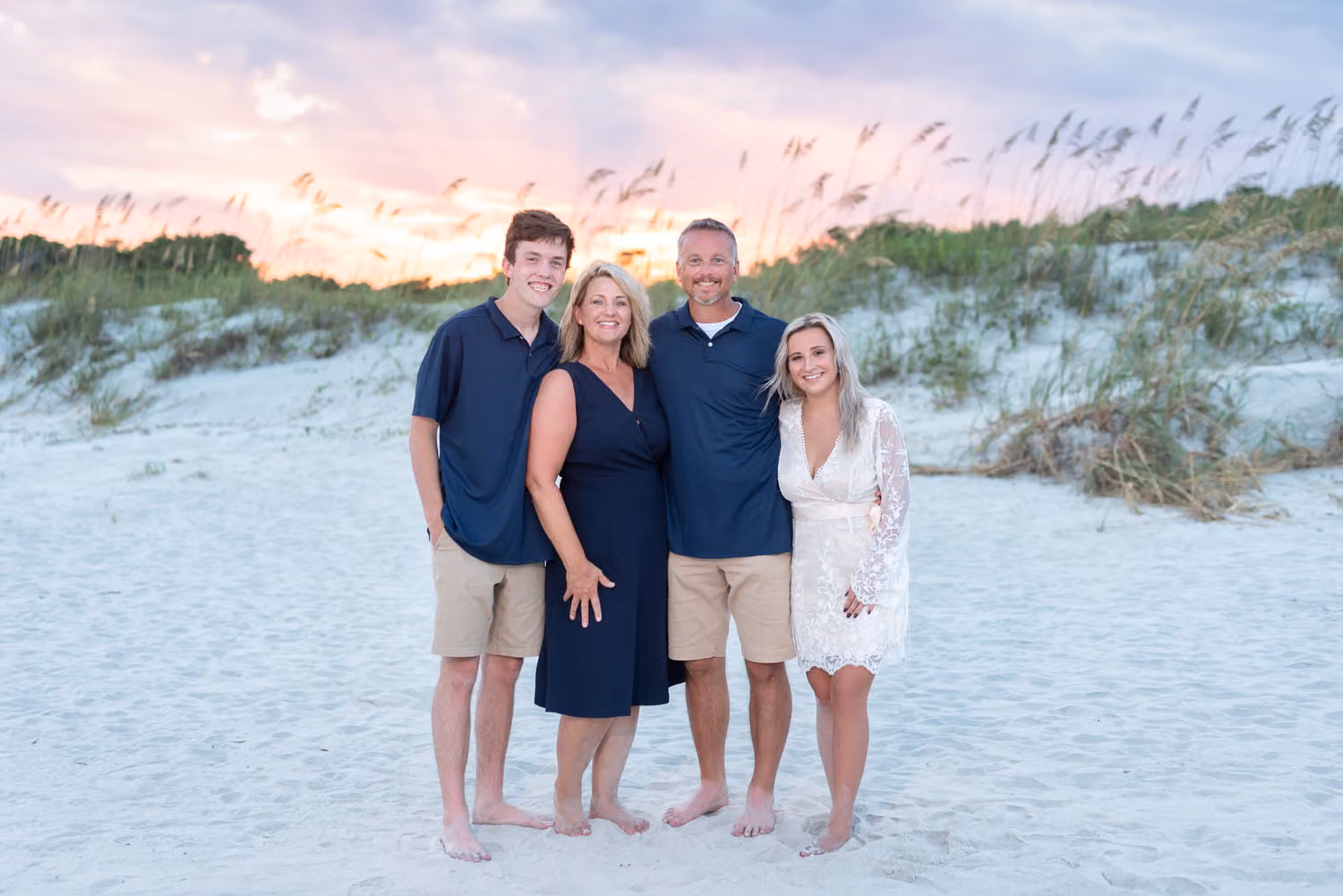 Family of four standing by the sea oats under a pink and purple sunset sky at Huntington Beach State Park