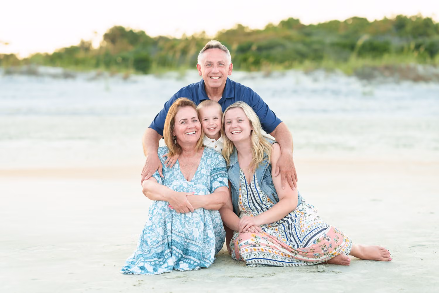 Grandparents sitting in the sand with their daughter and little grandson tucked between them at Huntington Beach State Park