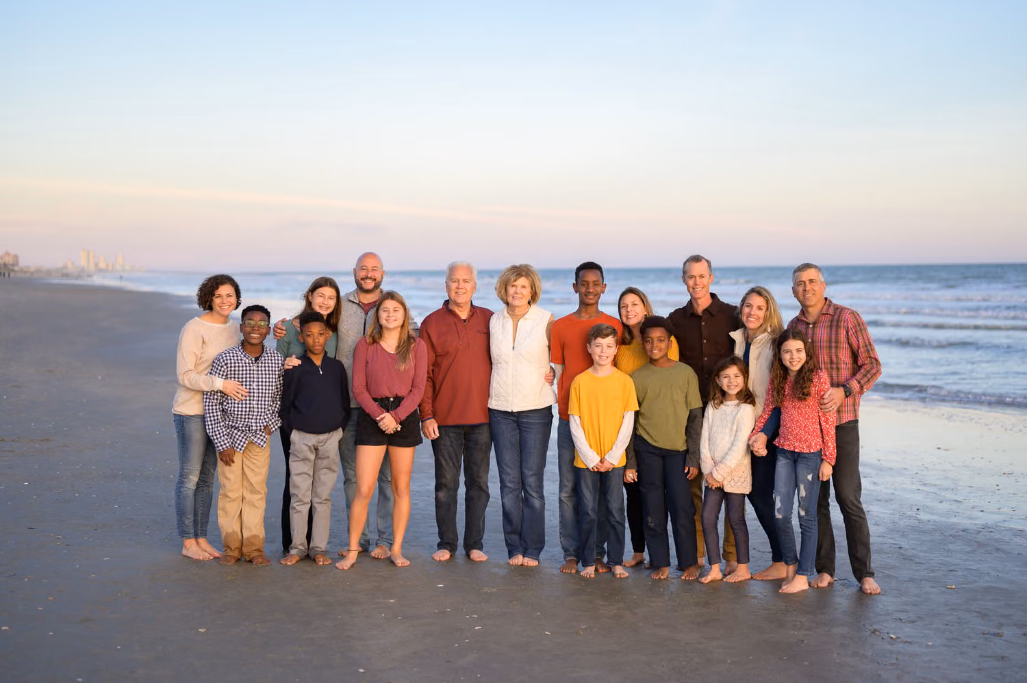 Extended family of about twenty standing together by the ocean in soft evening light in North Myrtle Beach