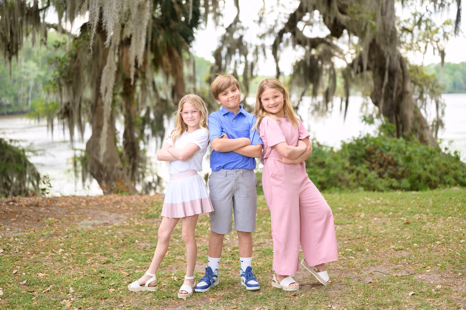 Boy with arms crossed between two girls on the lawn under mossy oaks by the water at Wachesaw Plantation