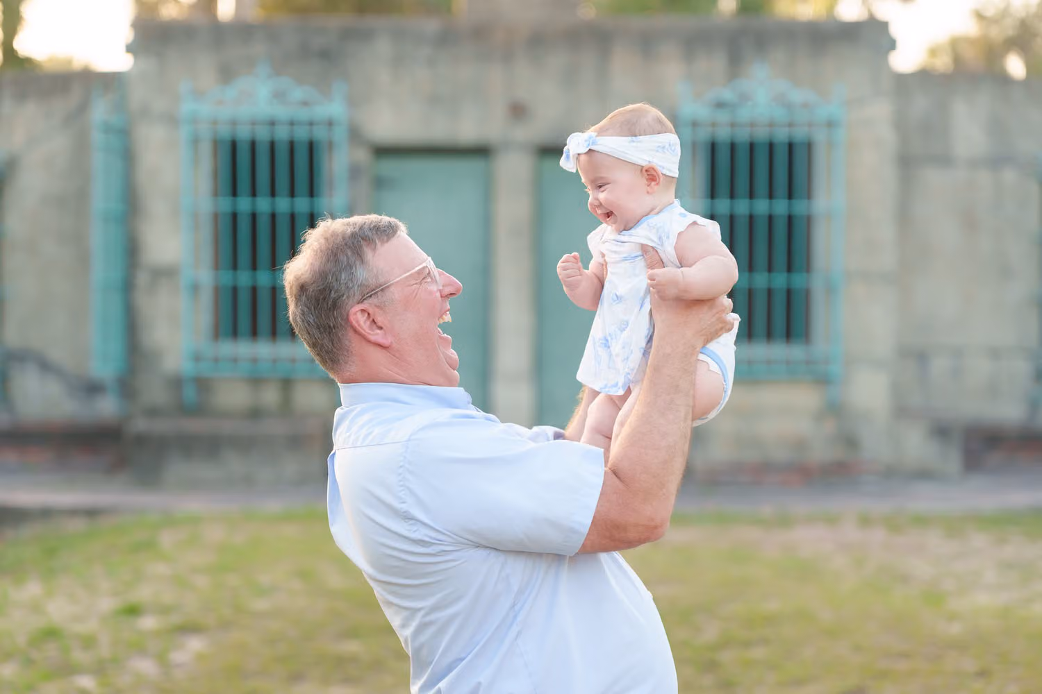 Grandfather lifting his smiling baby granddaughter in front of Atalaya Castle at Huntington Beach State Park