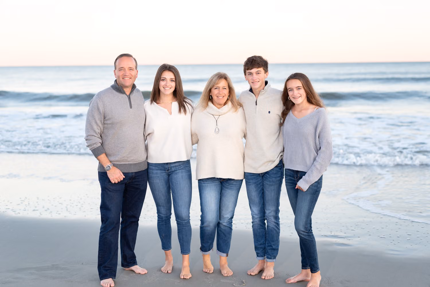 Parents and their three adult children in jeans and sweaters standing at the water's edge at Huntington Beach State Park