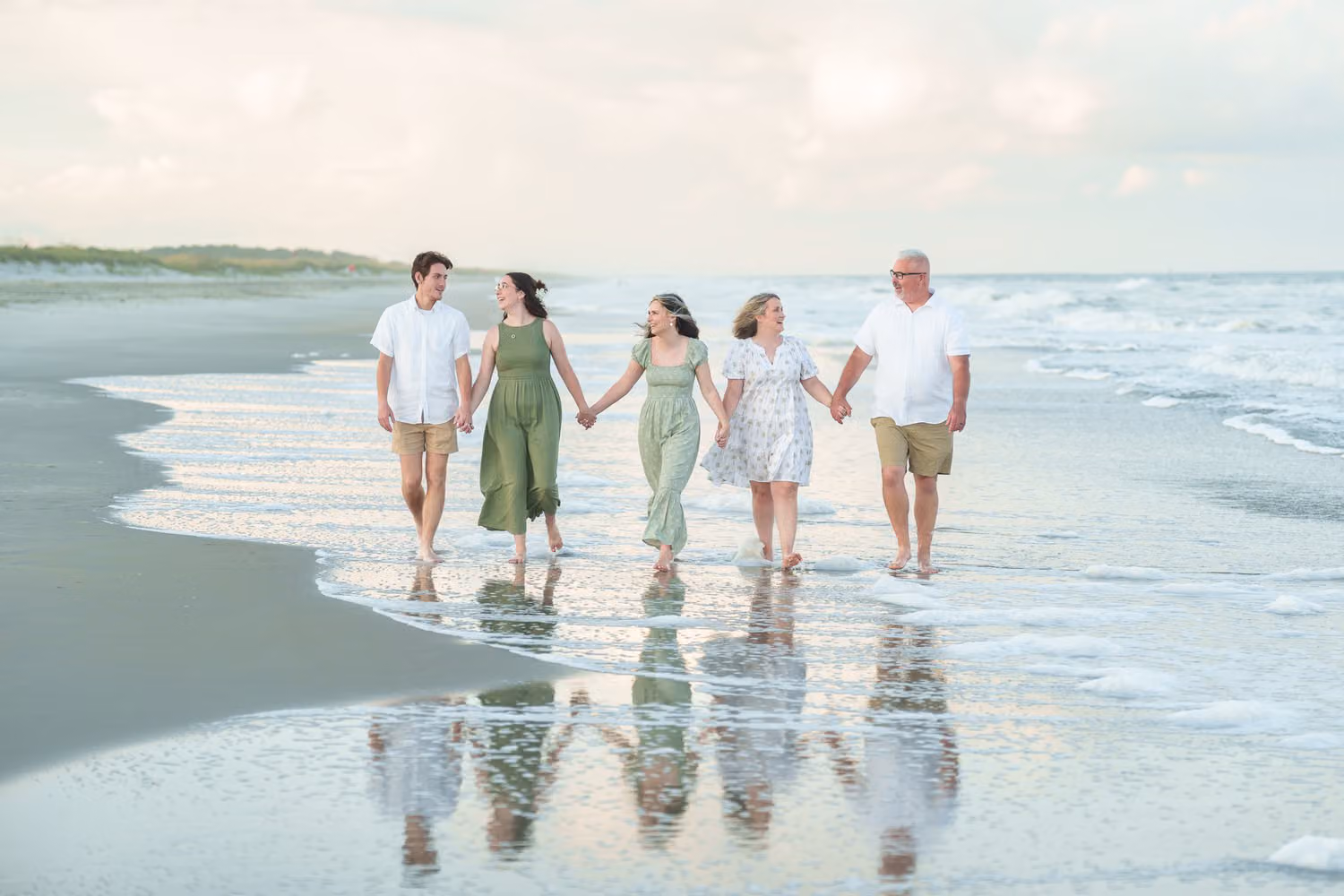 Family of five holding hands and walking through shallow water with their reflections below at Huntington Beach State Park