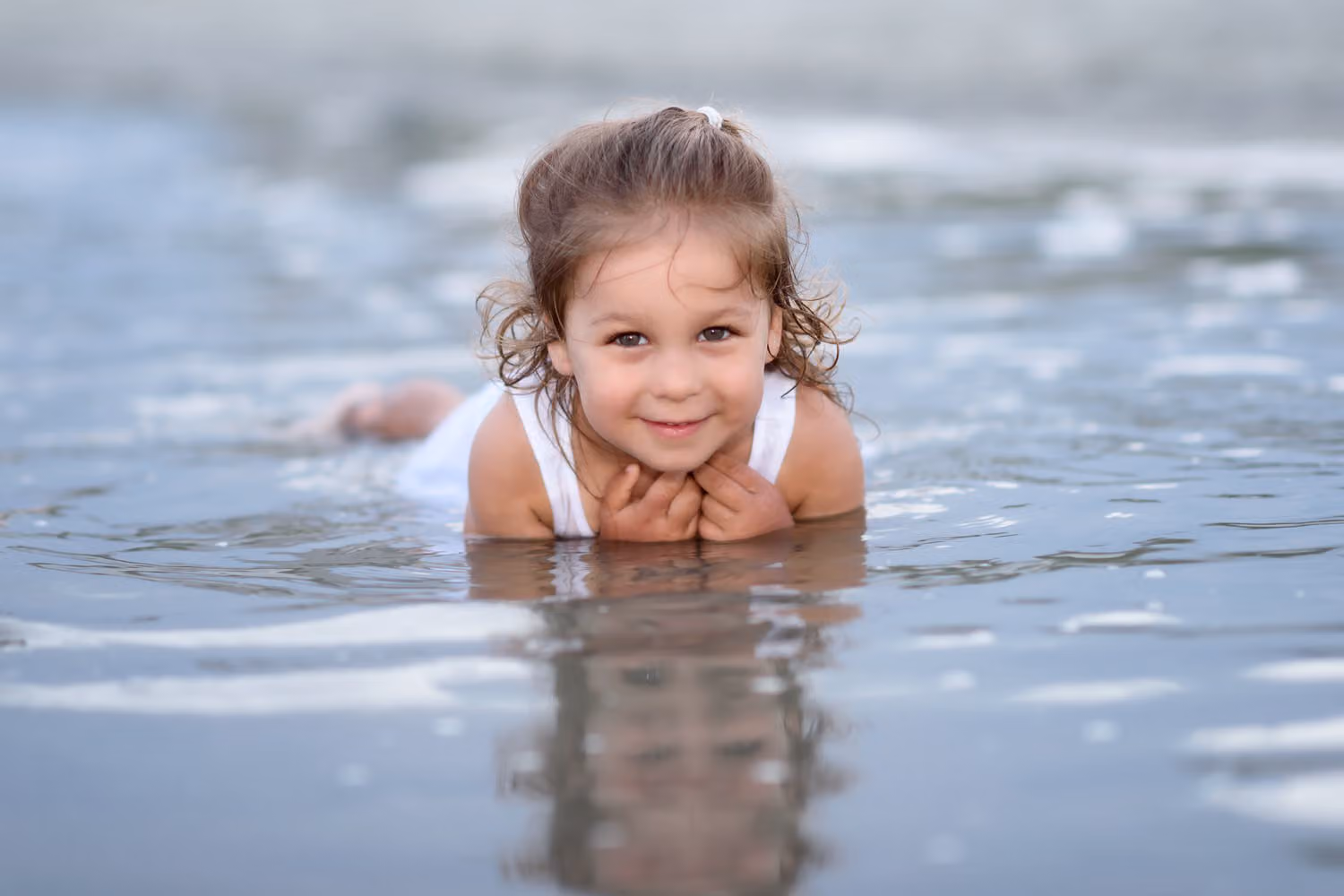 Smiling little girl lying in the shallow water with her chin on her hands in North Myrtle Beach
