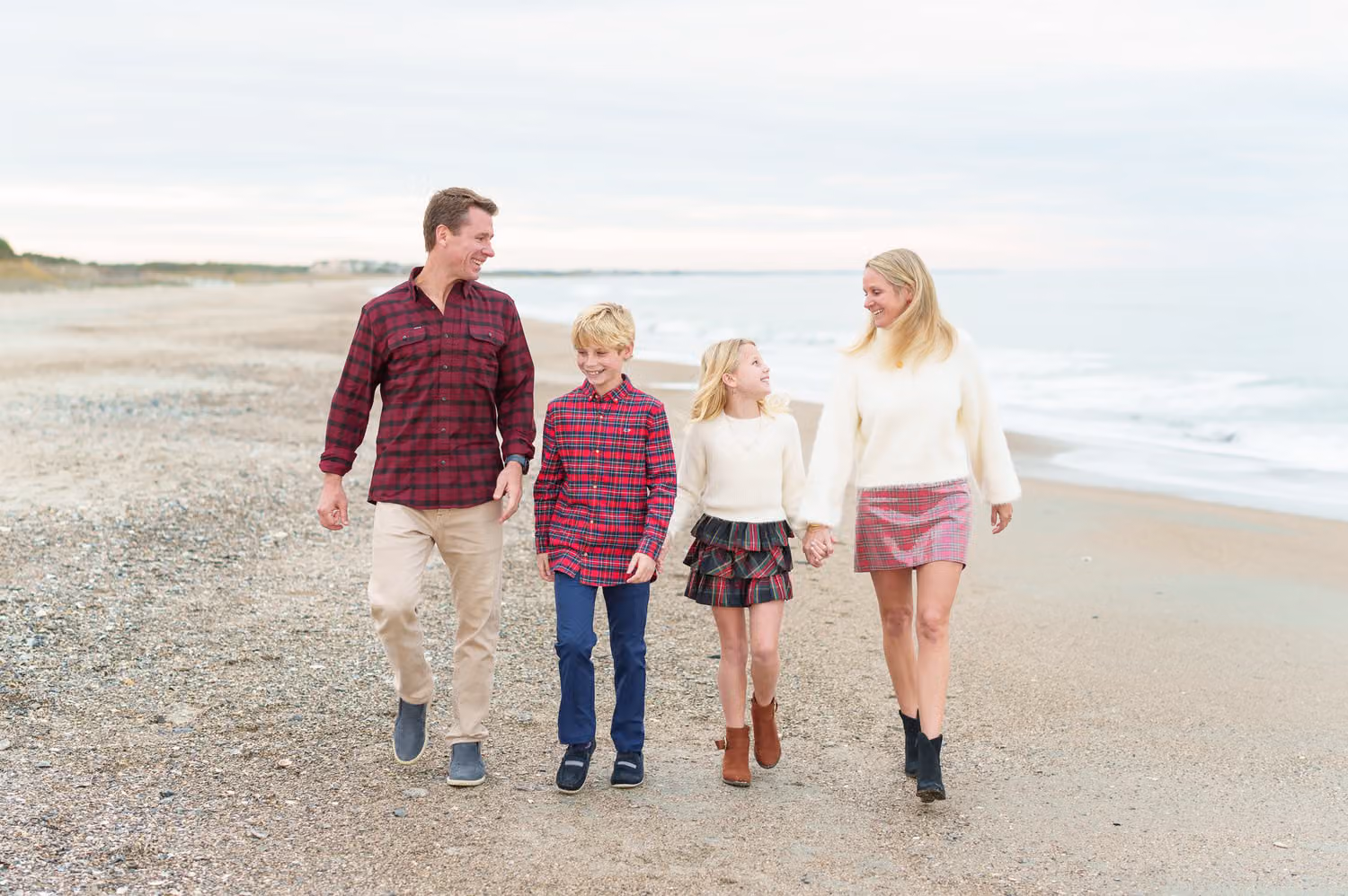 Family of four in fall sweaters and boots walking together along the beach at Debordieu