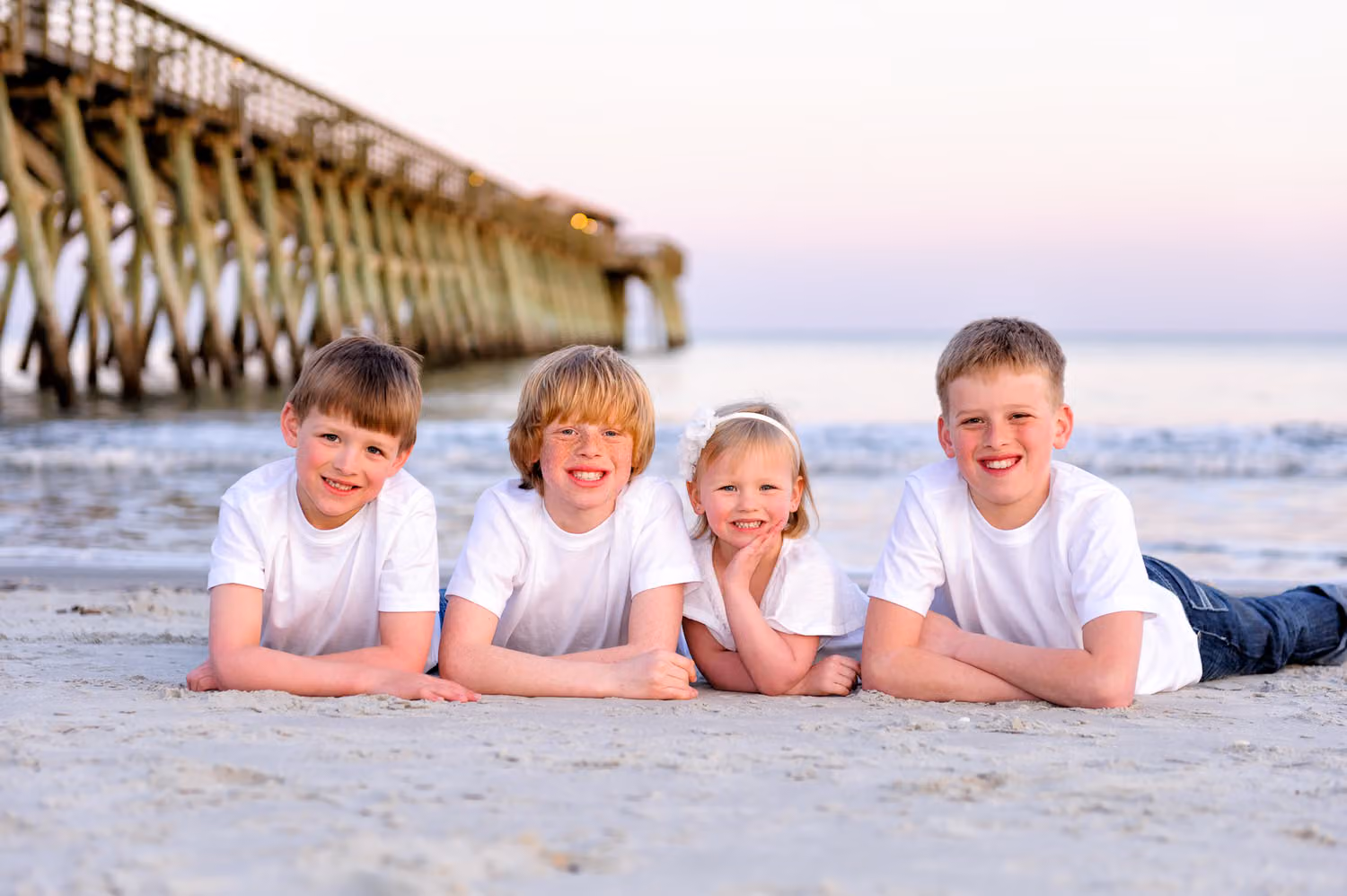 Three brothers and their little sister lying on their stomachs in the sand beside the pier in Myrtle Beach