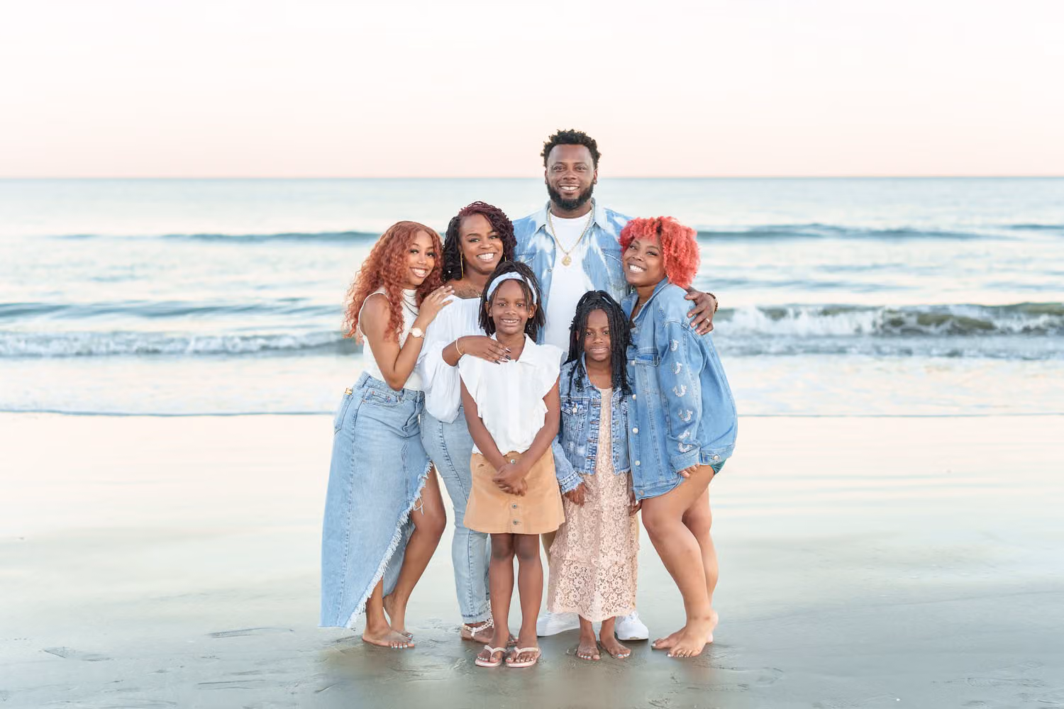 Parents with their four daughters in denim and white standing together by the ocean at Huntington Beach State Park