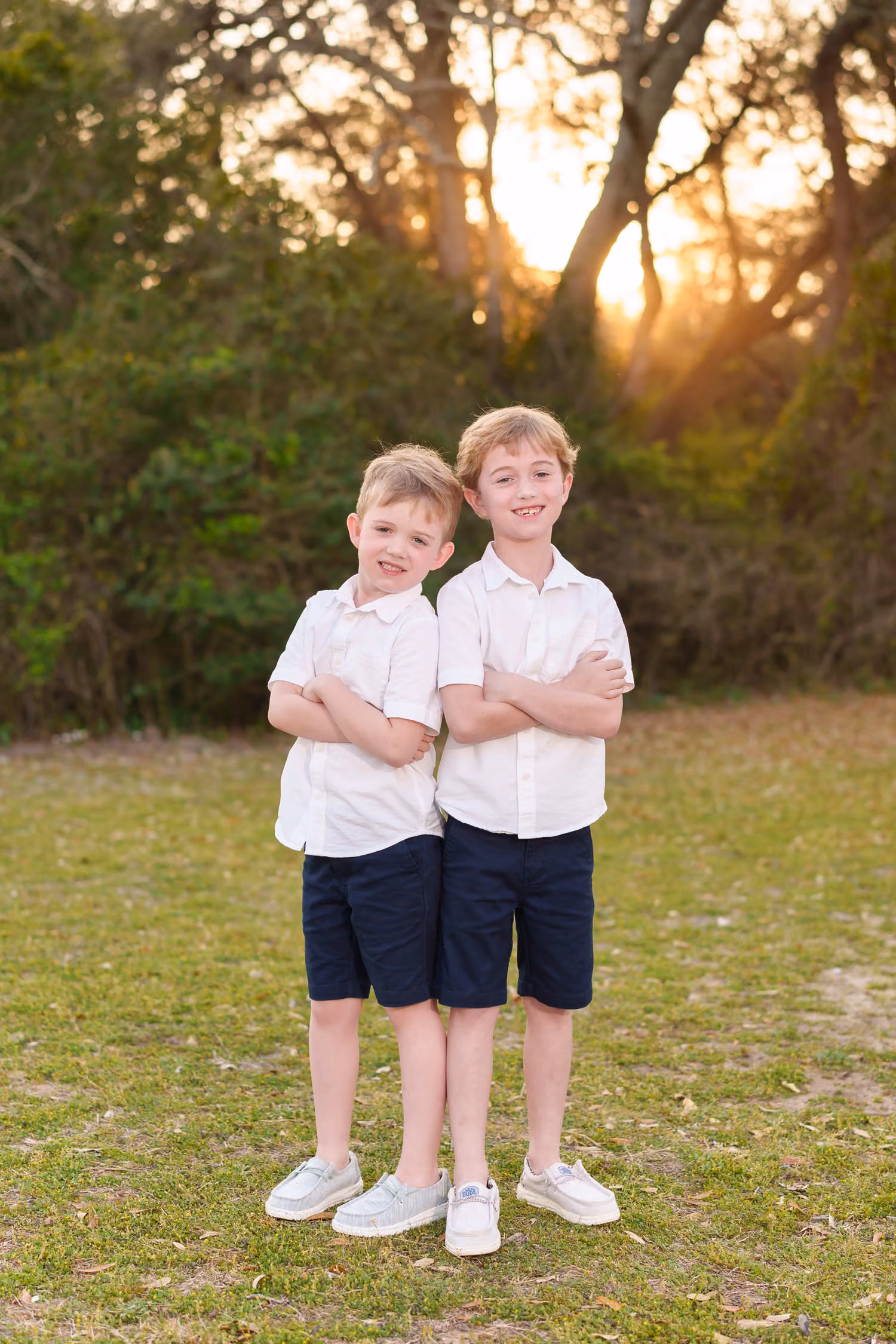Two little brothers in white shirts standing arm in arm as the sun sets behind the trees at Myrtle Beach State Park