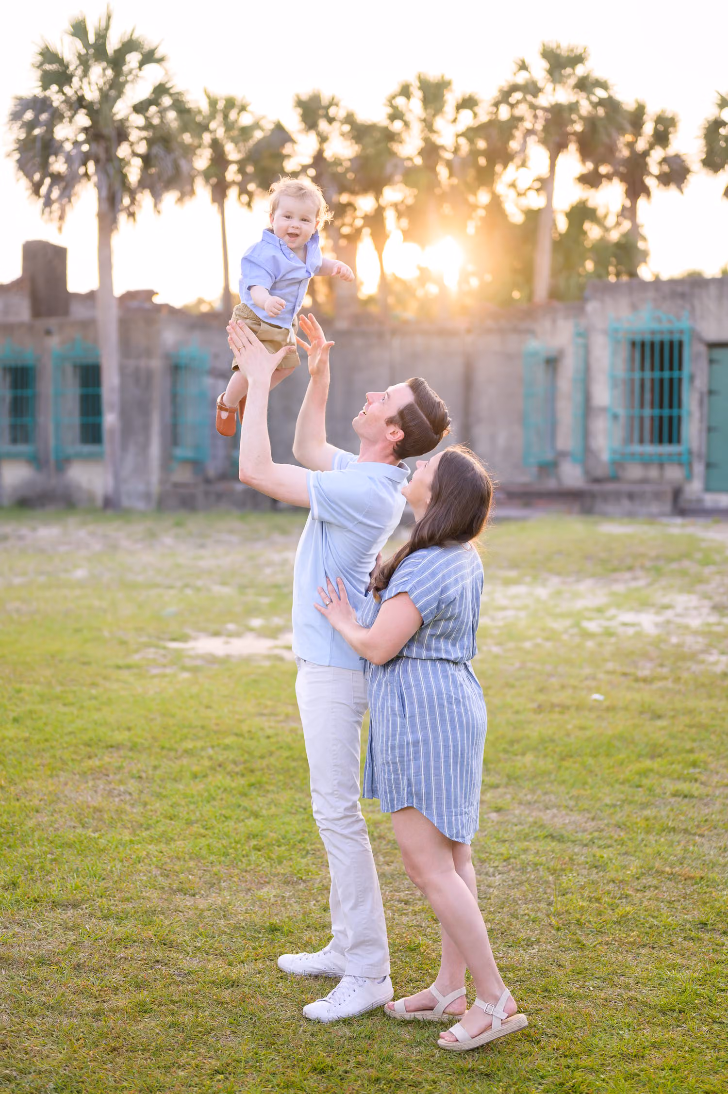 Dad tossing his little boy up as mom hugs him in front of the castle and palm trees at Huntington Beach State Park