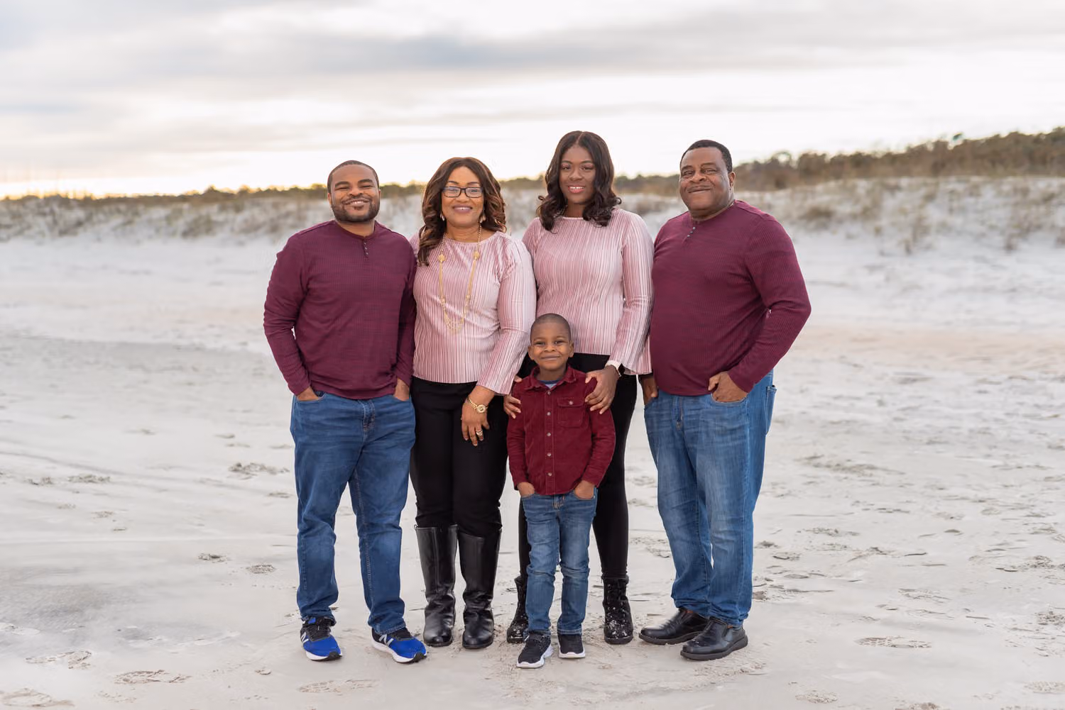 Family of five in maroon and pink standing together on the sand in front of the dunes at Huntington Beach State Park