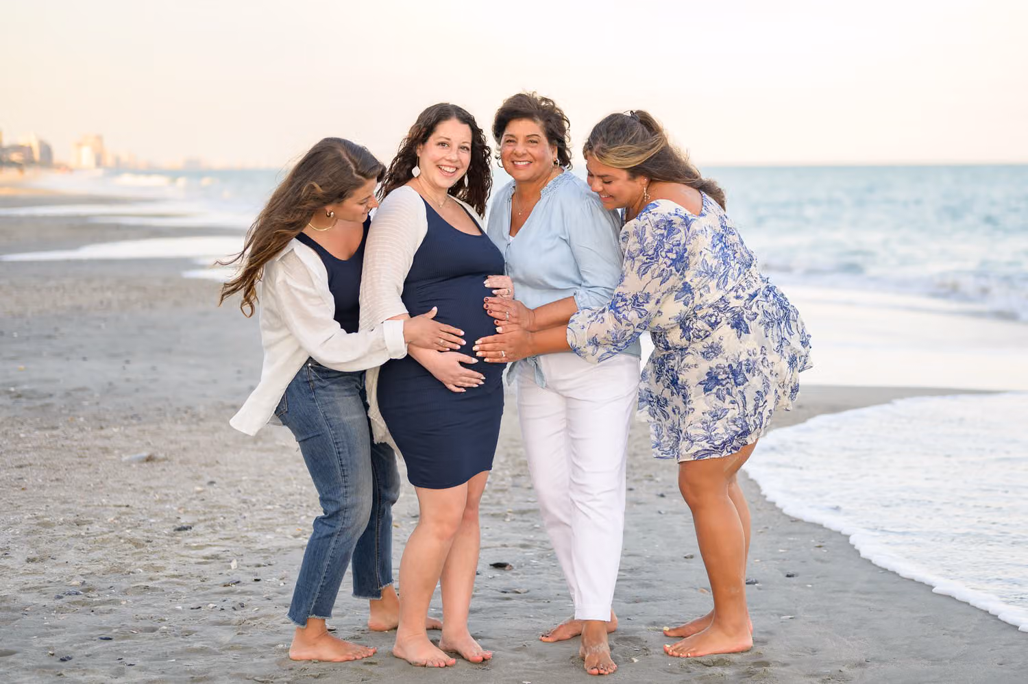 Sisters and their mom gathered around an expectant mother, hands on her belly, on the beach at Island Vista Resort