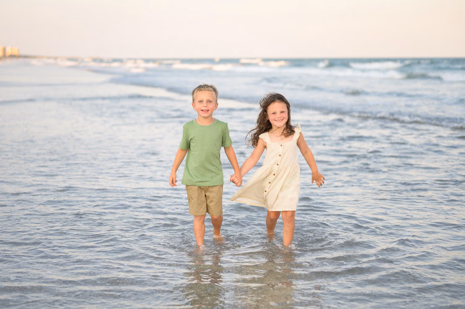 Little boy and girl walking hand in hand through shallow water with Cherry Grove Pier behind them