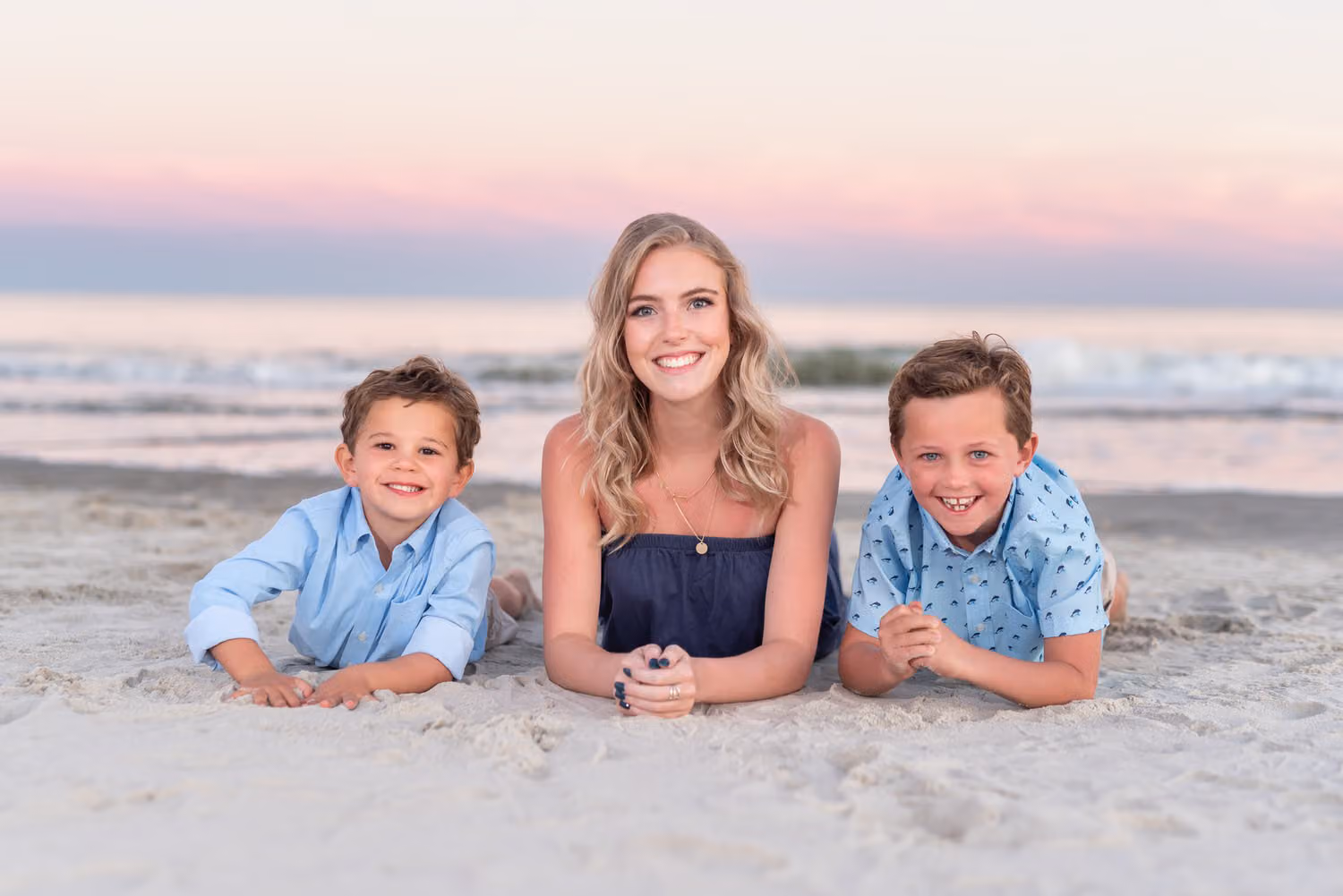 Teen girl lying in the sand between two little boys at sunset at Huntington Beach State Park