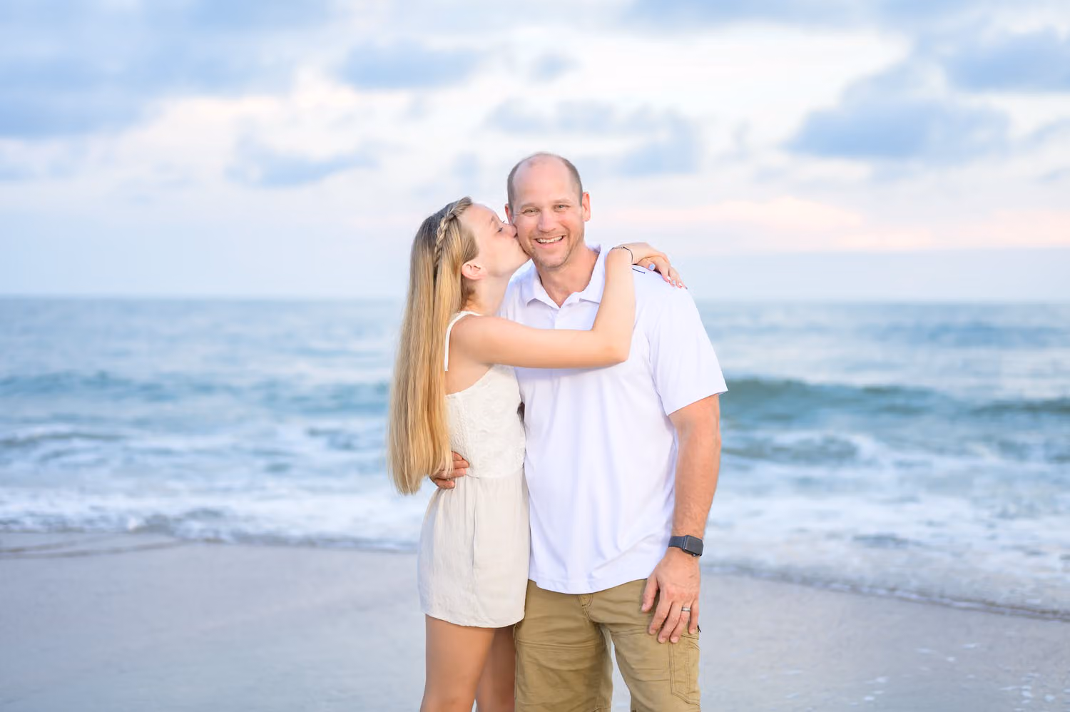 Woman kissing her husband's cheek as they stand on the beach in front of the waves at Huntington Beach State Park
