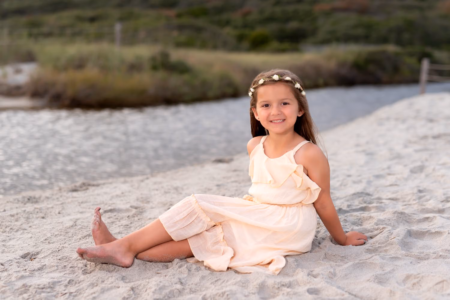 Little girl in a cream dress and flower crown sitting in the sand by the beach path at Myrtle Beach State Park