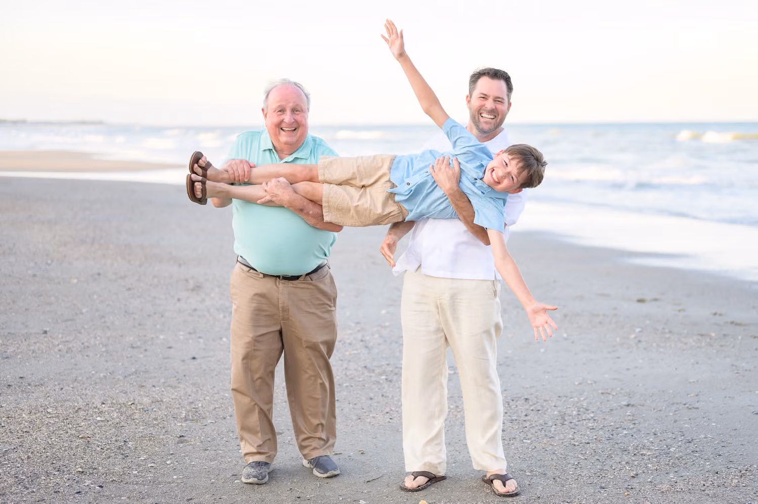 Grandfather and dad holding a little boy flat like Superman with arms out on the beach in Pawleys Island