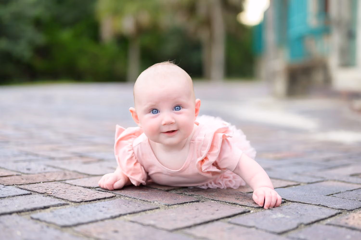 Smiling baby girl in pink lying on her tummy on brick pavers near the castle at Huntington Beach State Park