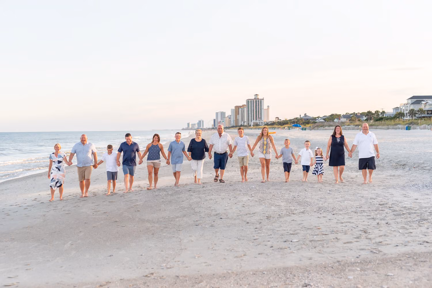 Large family holding hands as they walk along the shore with high-rise hotels behind them in Myrtle Beach