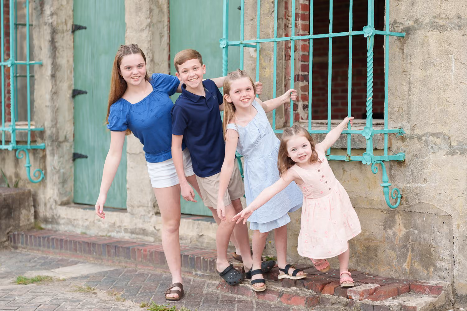 Four siblings posing and reaching out from the teal window grates of the Atalaya Castle at Huntington Beach State Park