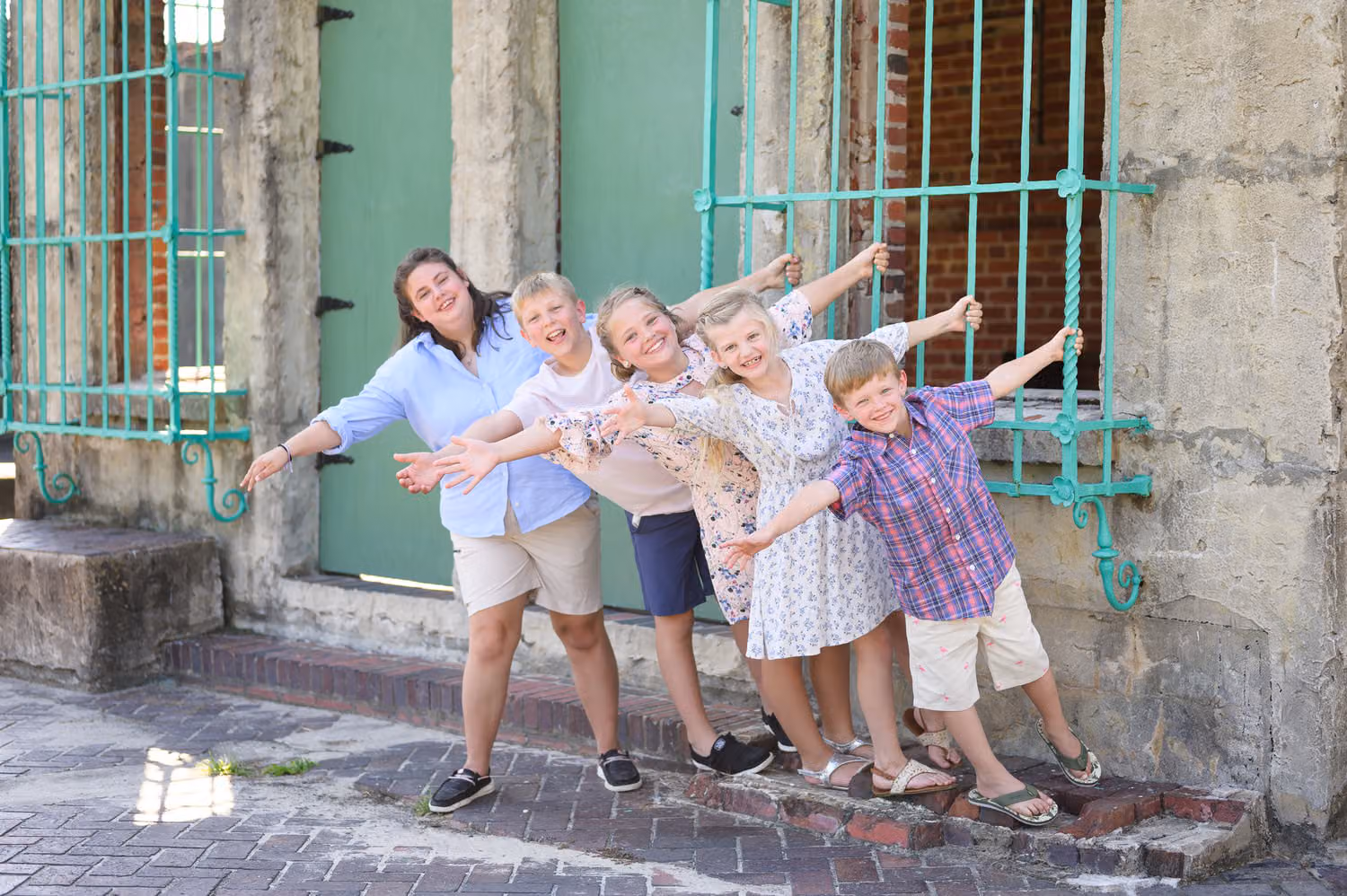 Cousins posing with arms out by the barred window and teal doors at Atalaya Castle, Huntington Beach State Park
