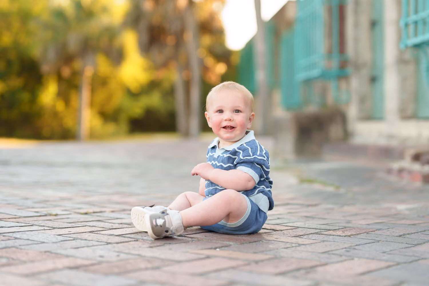 Smiling baby boy sitting on a brick walkway beside the teal windows of the Atalaya Castle at Huntington Beach State Park