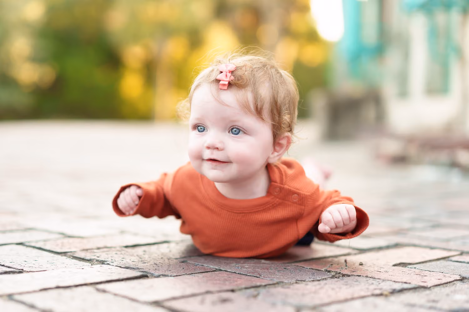 Baby girl in a rust sweater lying on her tummy on brick pavers with arms out near the castle at Huntington Beach State Park