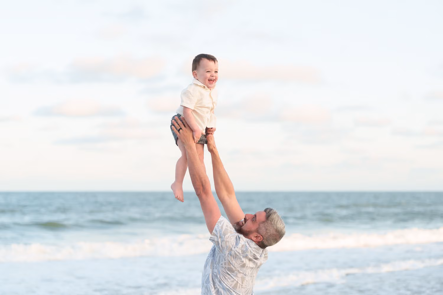 Dad lifting his laughing little boy high above his head by the ocean at Huntington Beach State Park