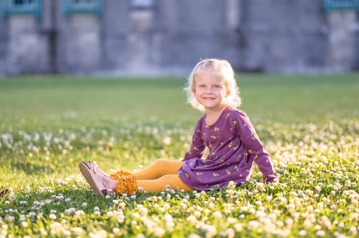Toddler girl in a purple dress sitting in the clover in front of the castle at Huntington Beach State Park