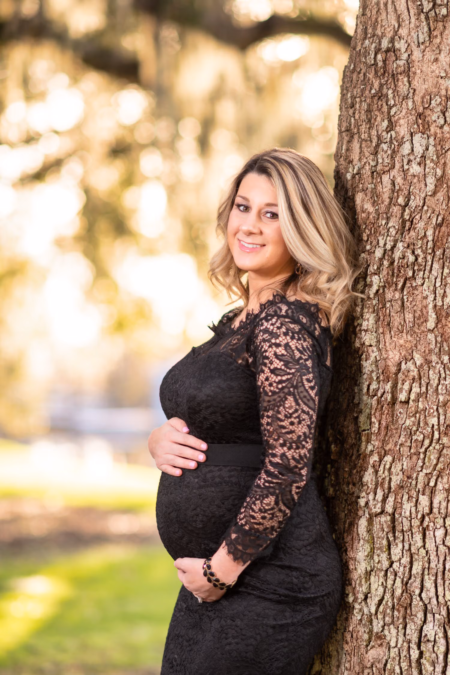 Expectant mother in black lace leaning against an oak trunk with Spanish moss behind her at Caledonia Golf & Fish Club