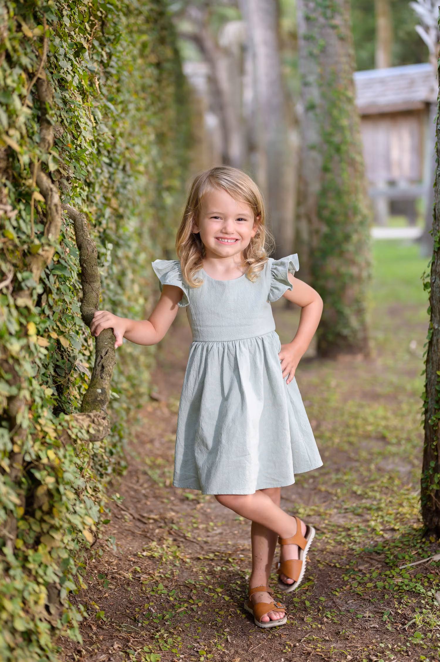 Little girl in a sage dress and boots posing against the ivy wall beside a row of palms at Atalaya Castle