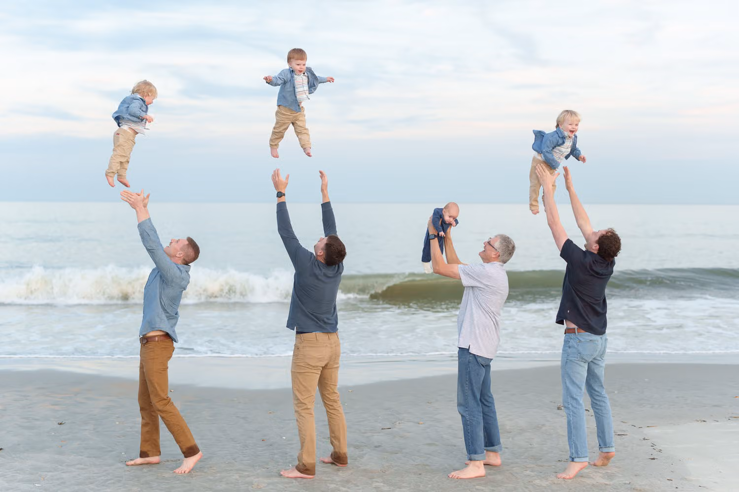 Four dads tossing their little boys high into the air by the ocean at Huntington Beach State Park