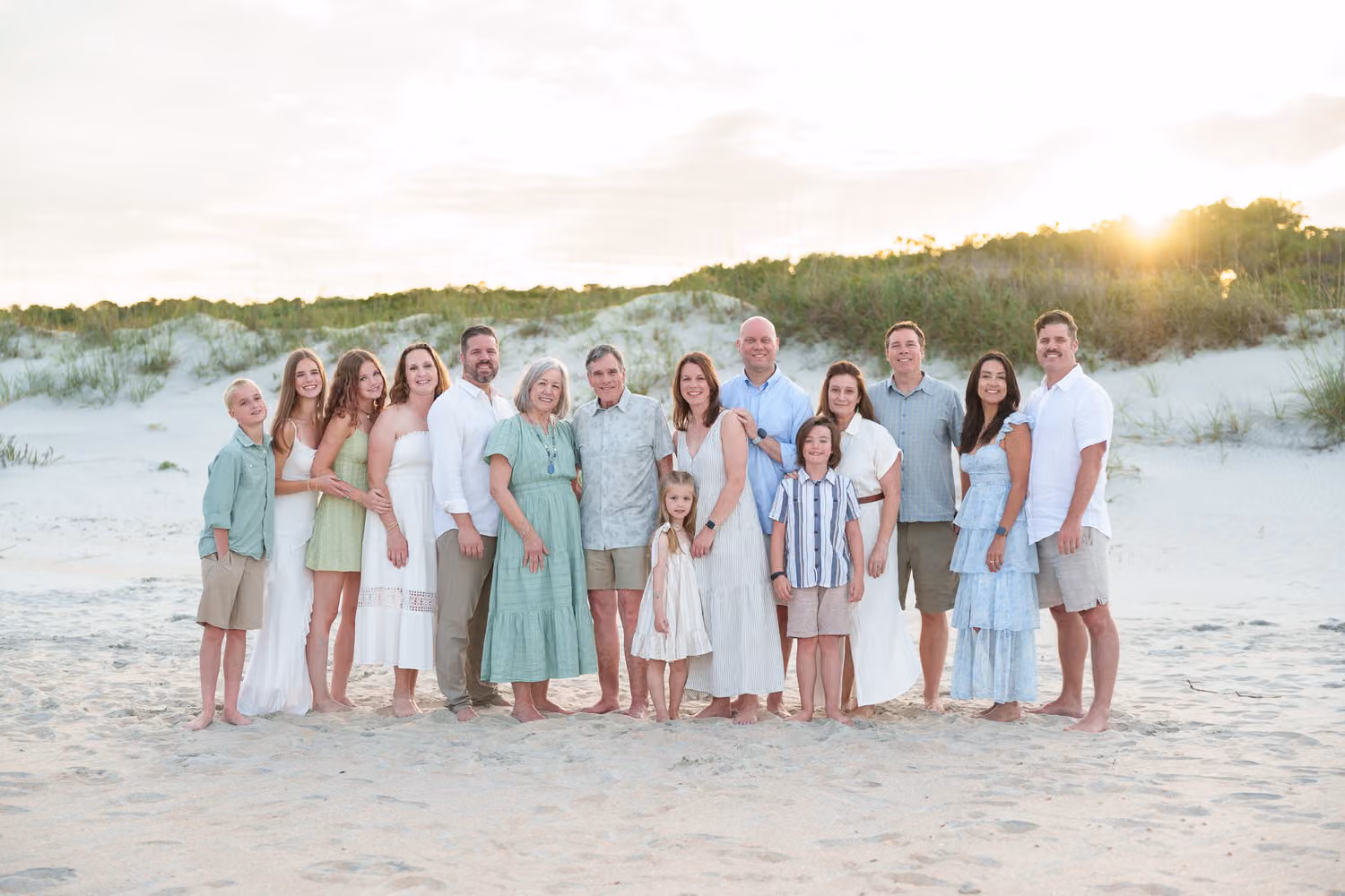Extended family in pastels standing on the sand by the dunes as the sun sets at Huntington Beach State Park