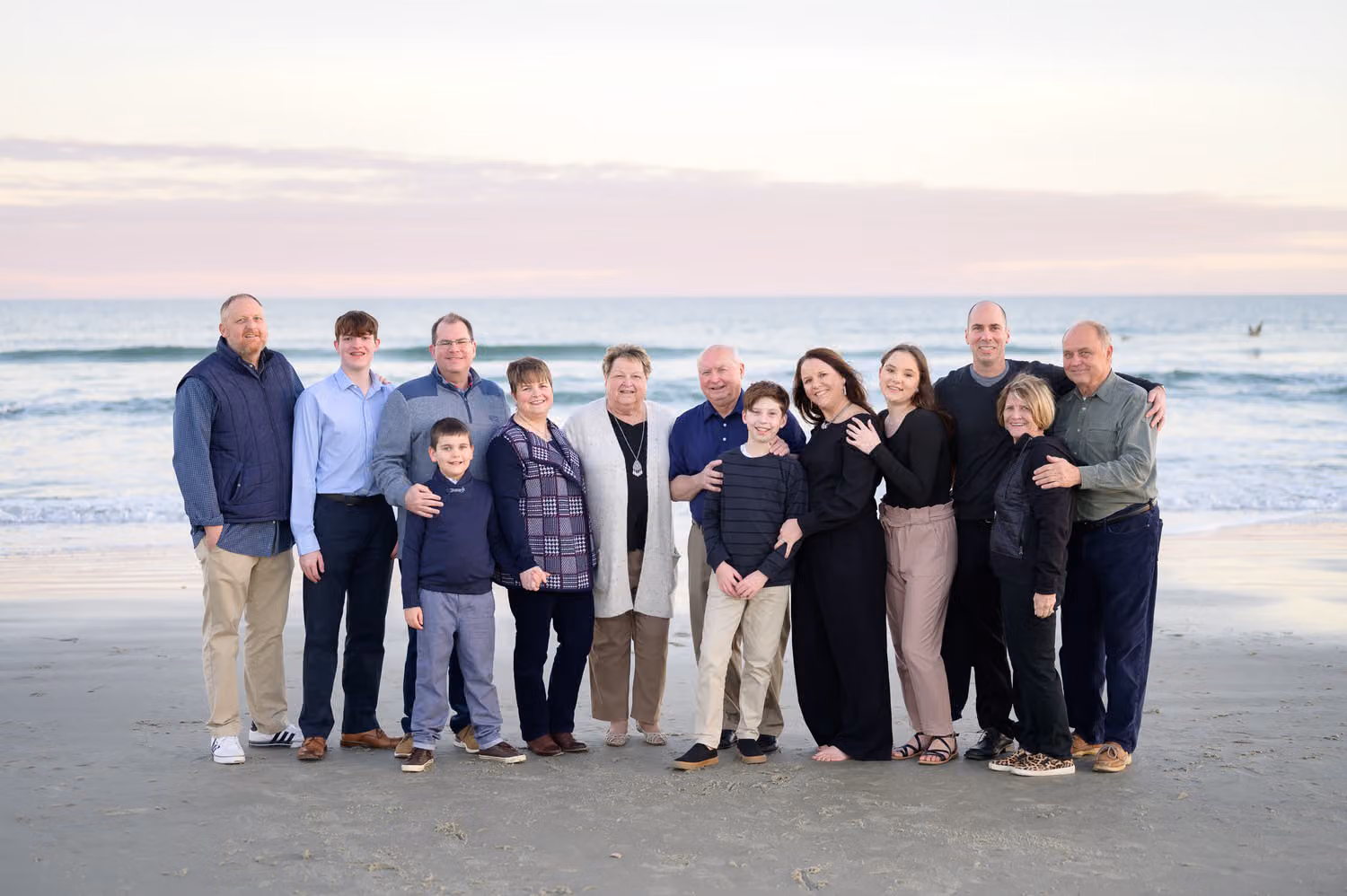 Grandparents with their large family in navy and gray standing by the ocean on a winter evening, Huntington Beach State Park