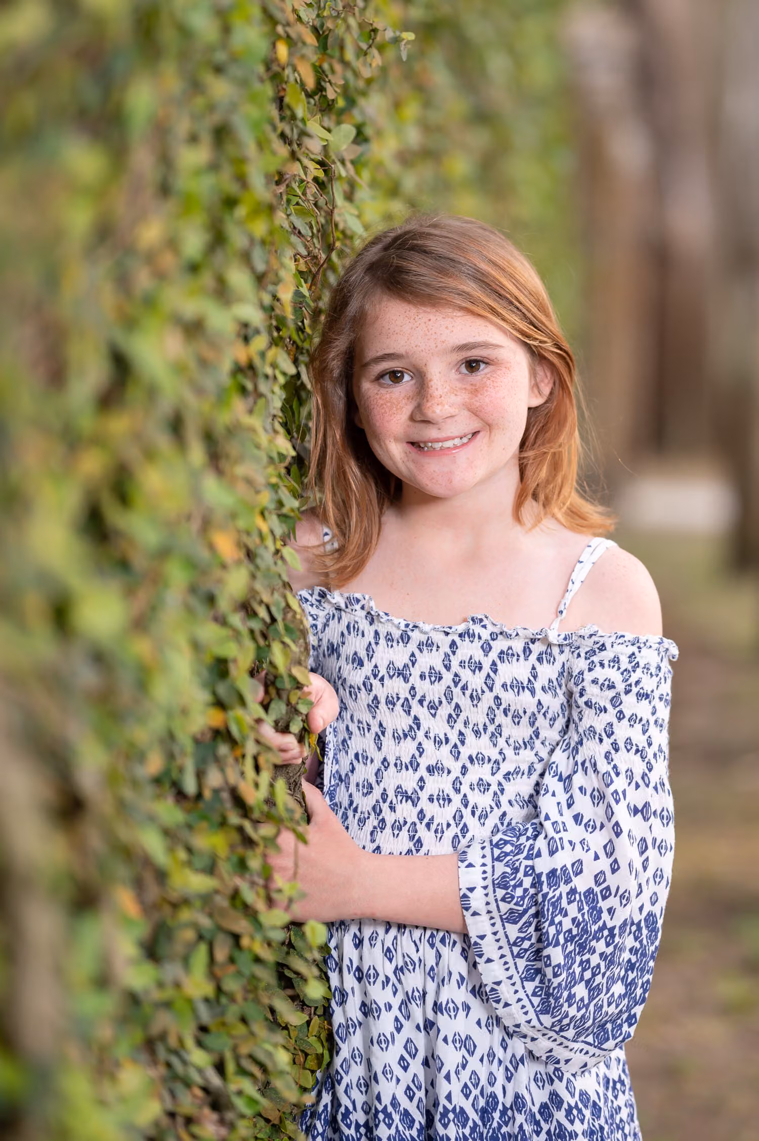 Smiling little girl in a blue and white dress leaning against the ivy-covered wall at Huntington Beach State Park