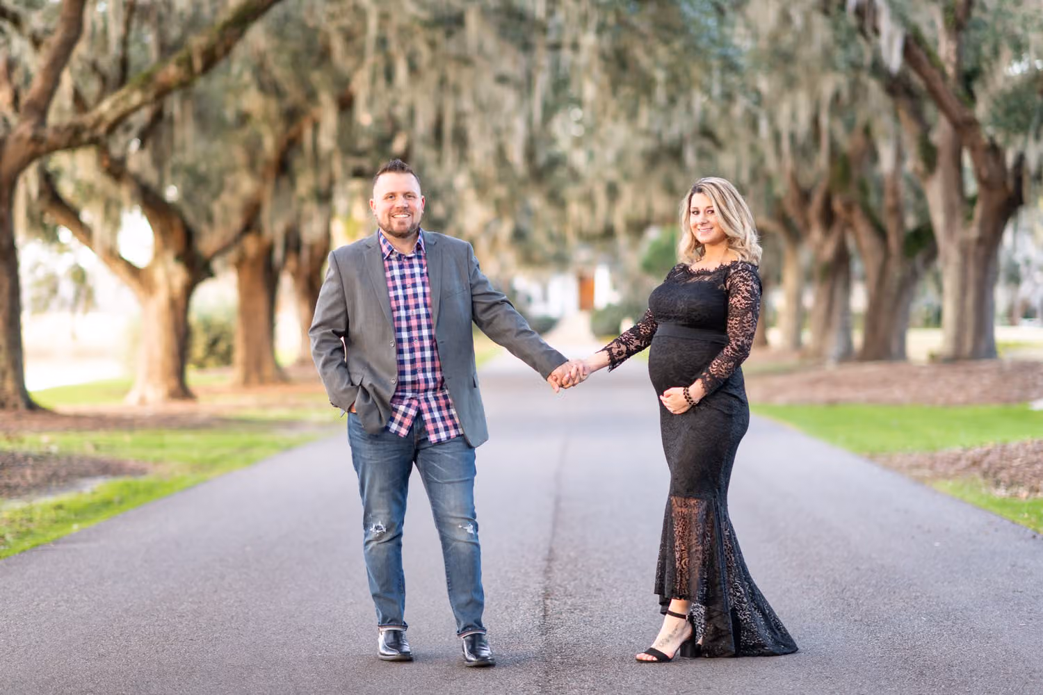 Expectant couple holding hands on the oak-lined avenue draped in Spanish moss at Caledonia Golf & Fish Club