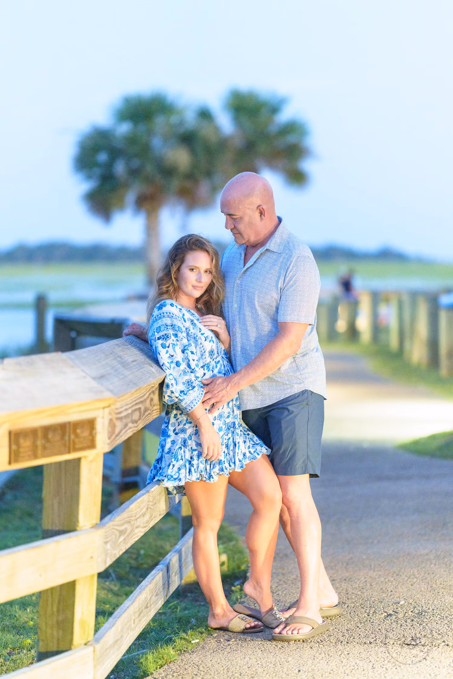 Couple leaning on a wooden railing under the evening streetlight with palms behind at the Marshwalk in Murrells Inlet