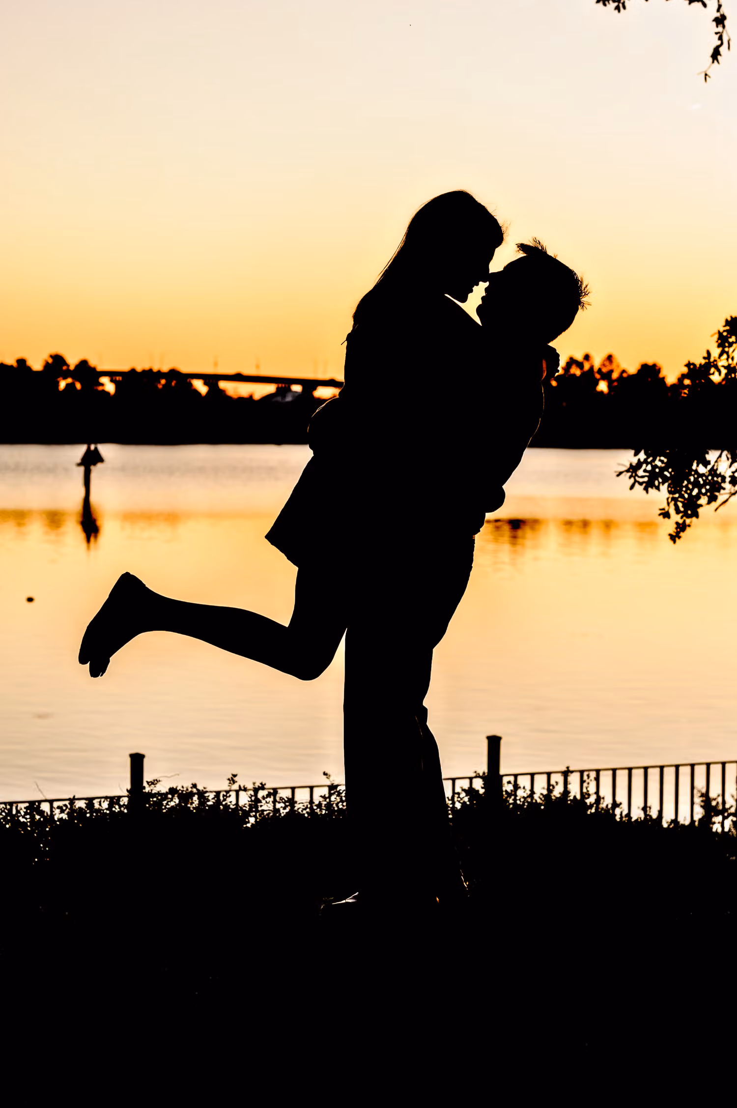 Silhouette of a couple kissing as she kicks up one leg against an orange sunset over the water in Downtown Georgetown