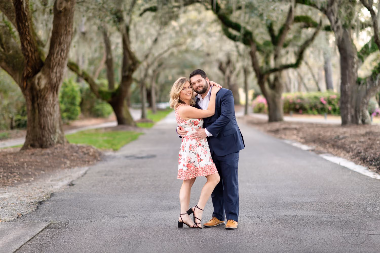 Woman wrapping her arms around her fiancé on a road lined with oak trees at Caledonia Golf & Fish Club