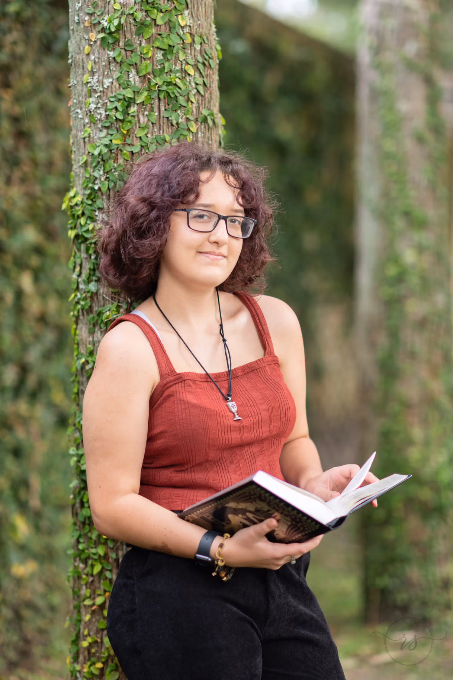 Senior with glasses holding an open sketchbook by an ivy-covered tree trunk at Huntington Beach State Park