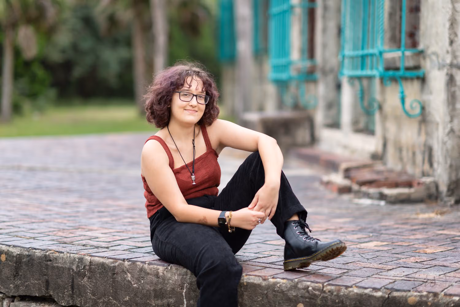 Senior in a rust top and black boots sitting on a brick ledge beside the castle at Atalaya Castle