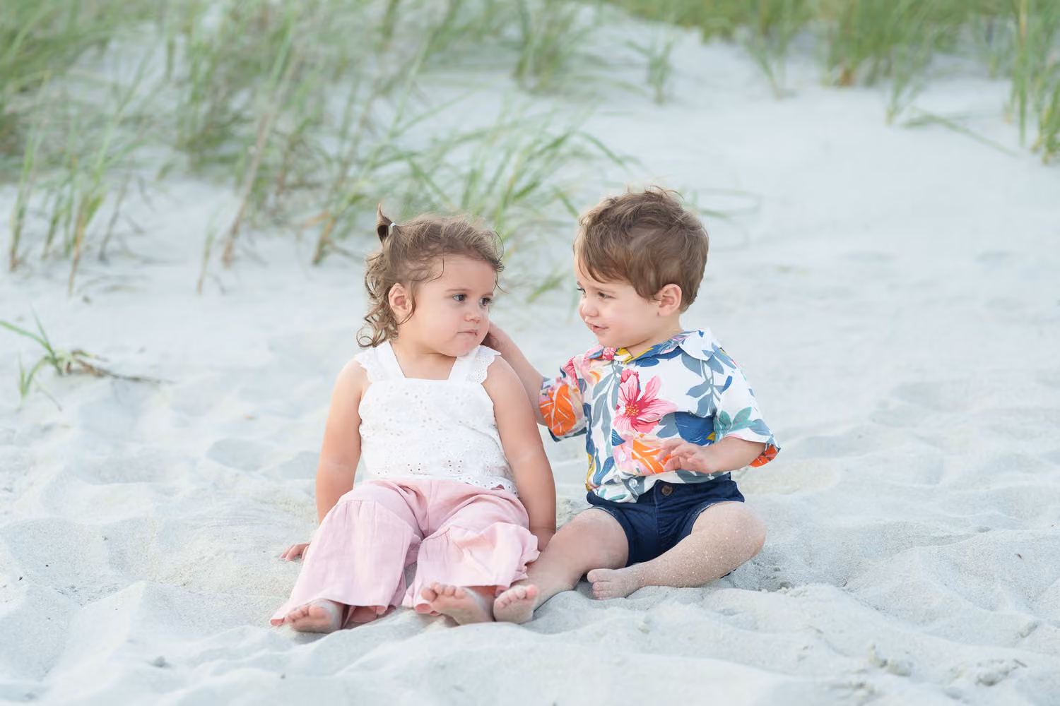 Toddler twins, a girl and a boy, sitting together in the sand by the dunes in Myrtle Beach