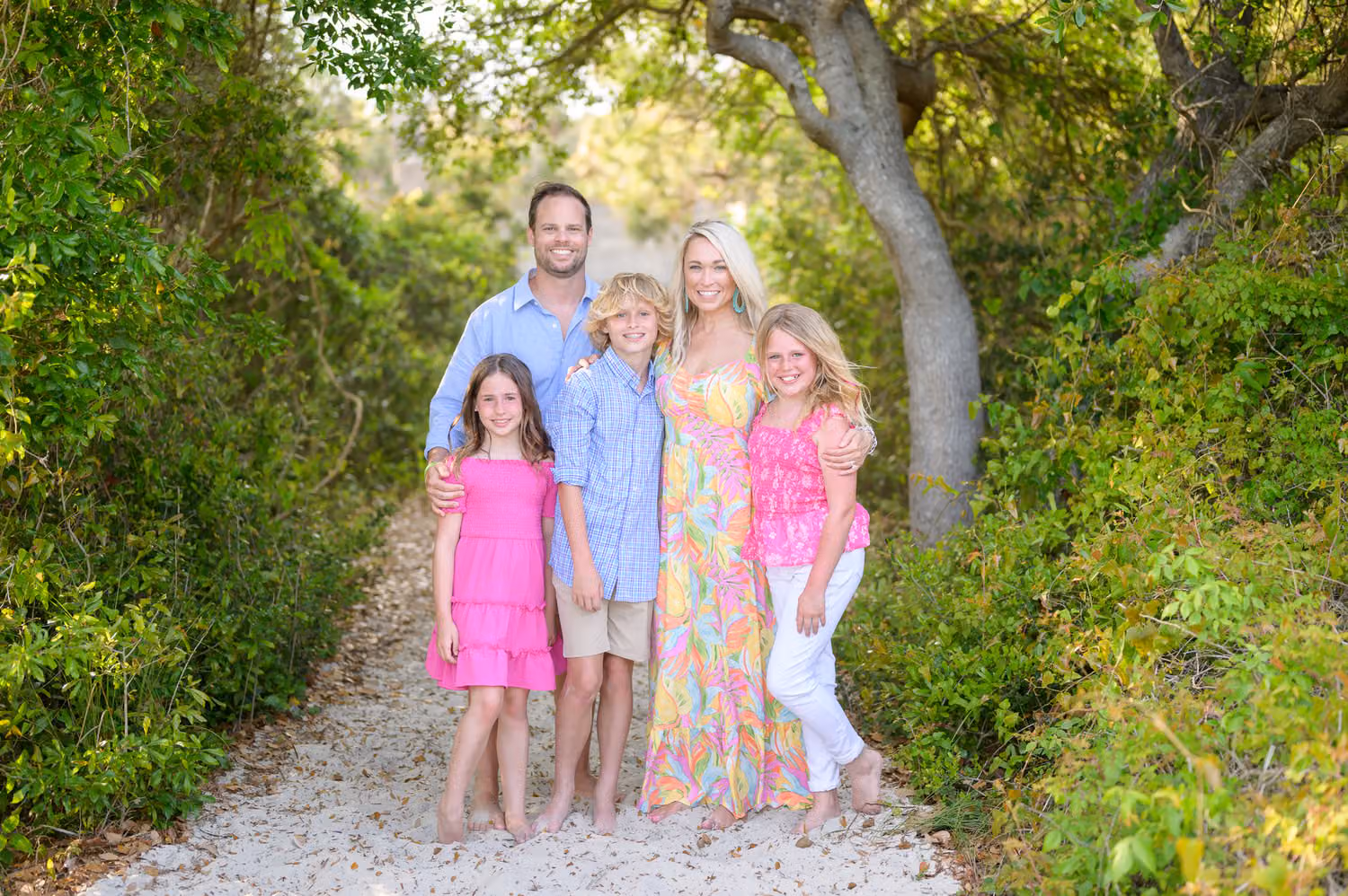 Family of five in pink and blue standing in the shade of the trees on the beach path at Huntington Beach State Park