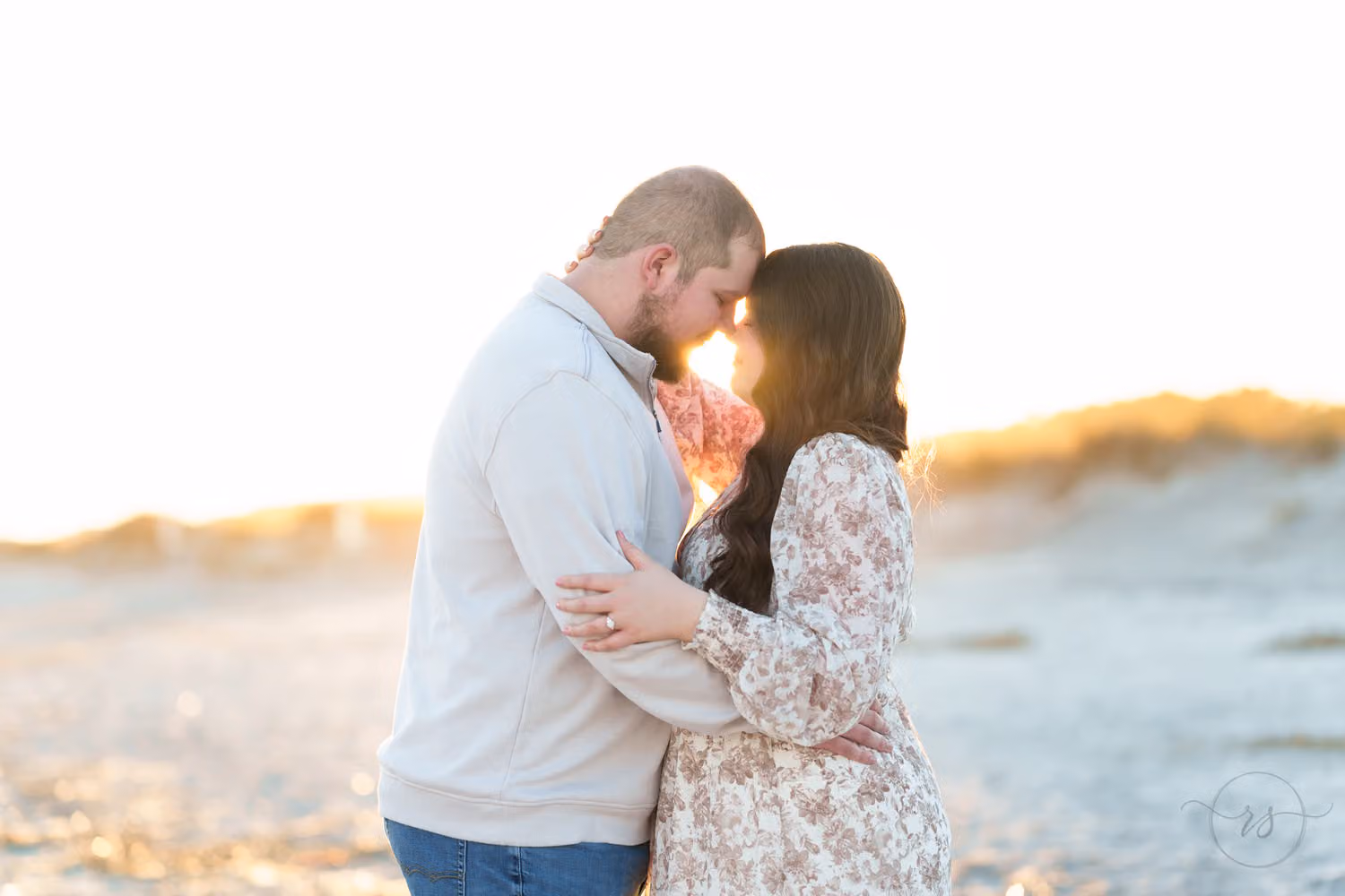 Couple touching foreheads as the setting sun glows behind them over the dunes at Huntington Beach State Park
