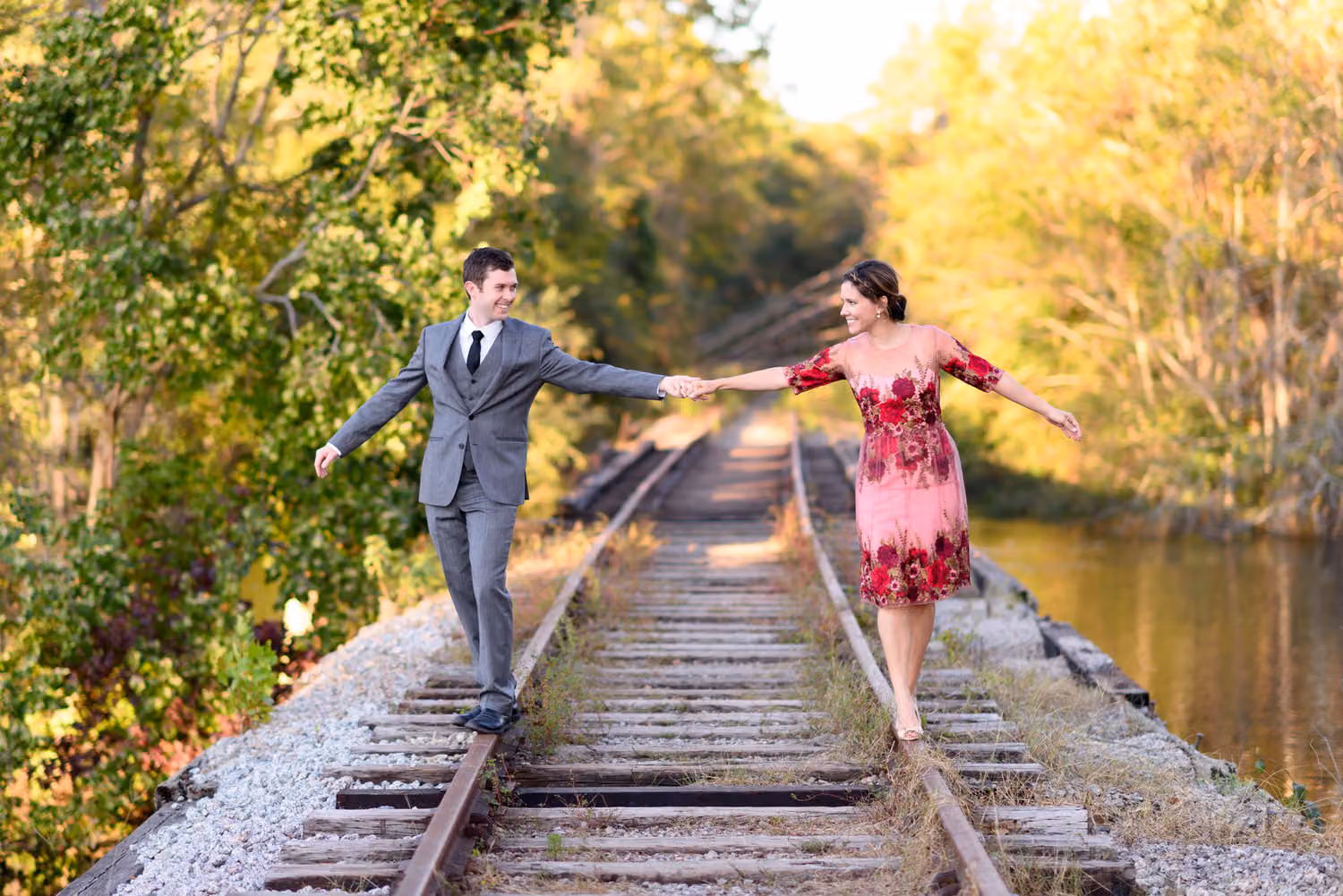 Arms out for balance, a couple walks hand in hand on the train track rails beside the river along the Conway Riverwalk