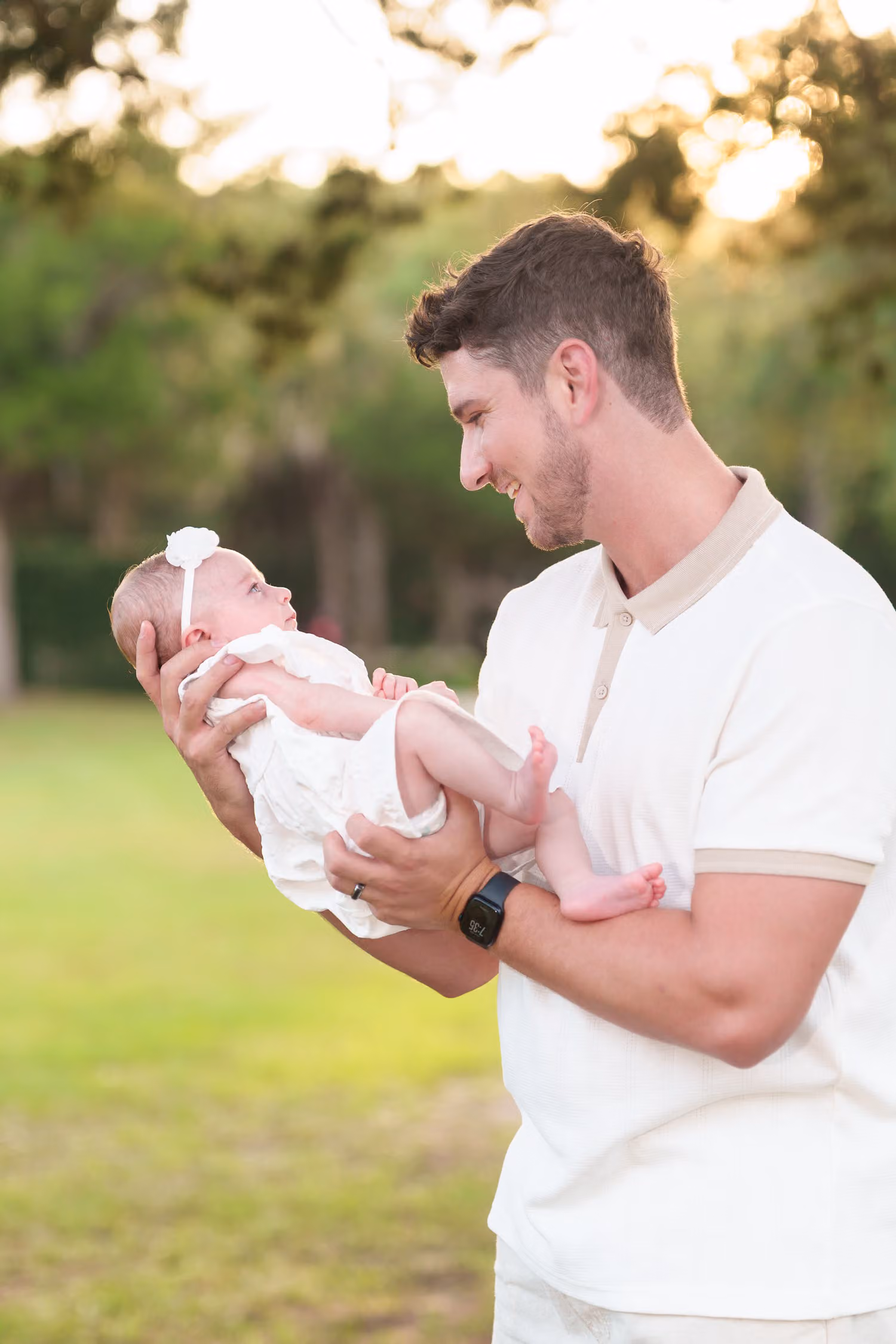 Father smiling down at his newborn daughter in his arms on a sunny lawn at Huntington Beach State Park